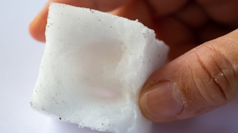 Close-up of fingers holding worn down melamine sponge