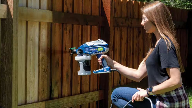 Woman using airless paint sprayer on fence