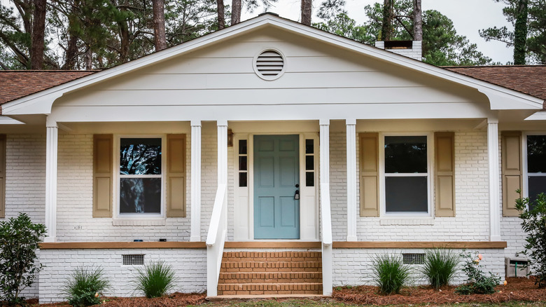 Ranch-style home with white painted brick and siding, beige shutters, and a blue front door.