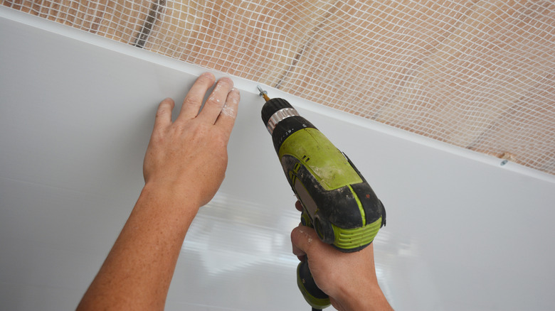 Person installing a ceiling panel with a drill