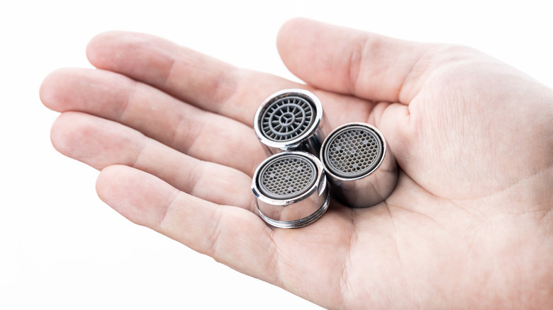 Hand holding differently sized faucet aerators 