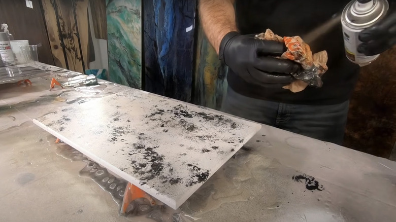 man spray painting plastic to dab canvas