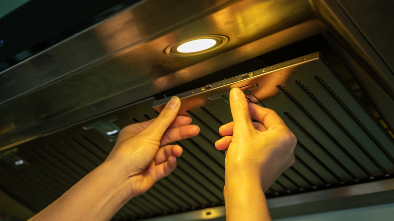 A woman's hands reaches to pull off a range hood filter