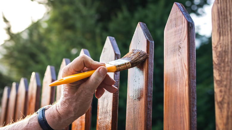 Person using a paint brush to stain a wooden fence