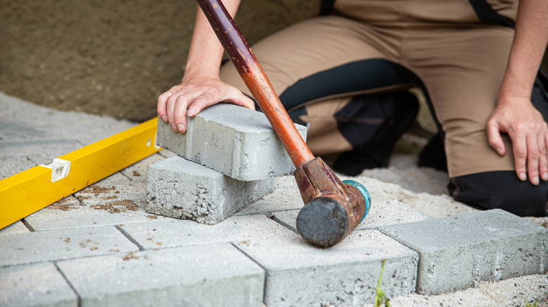 A person laying pavers for a fire pit area with a level and mallet