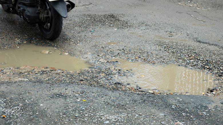 Two potholes filled with muddy water in a gravel driveway