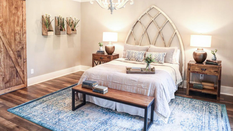 A white and cream bed with a repurposed window frame statement headboard sits on a blue rug