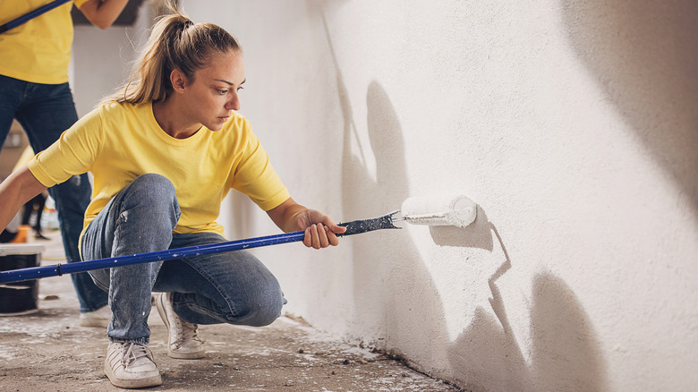 Woman crouched down painting a wall in the garage