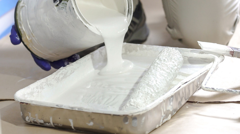 View of a hand pouring white paint into a roller tray