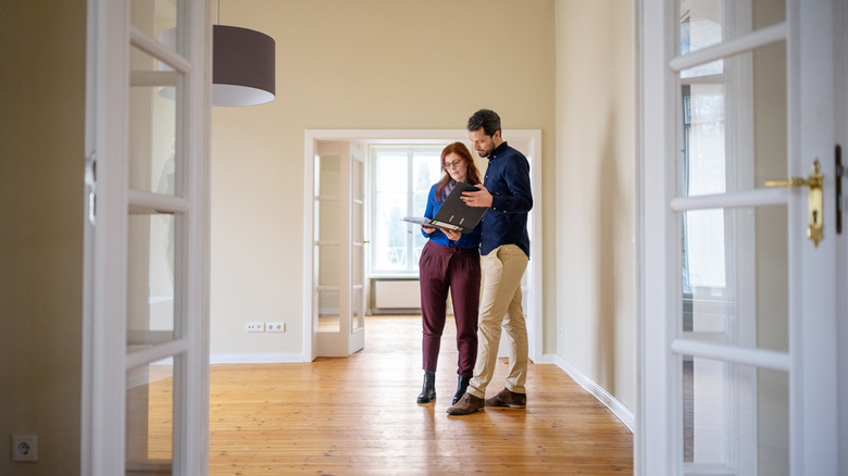 Man and woman consulting clipboard while standing in an empty living room