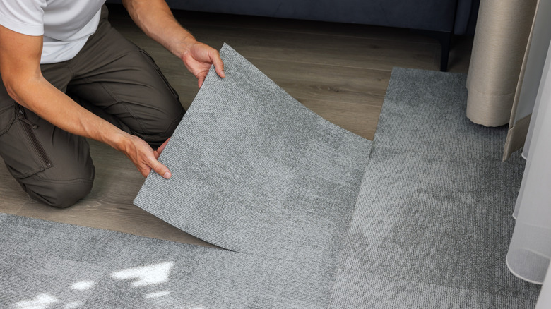 man installing self adhesive carpet tiles on floor