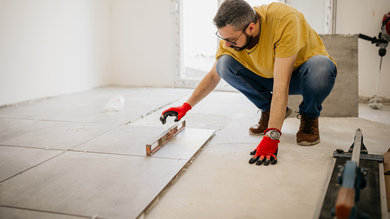 man checking floor tile installation, using a level