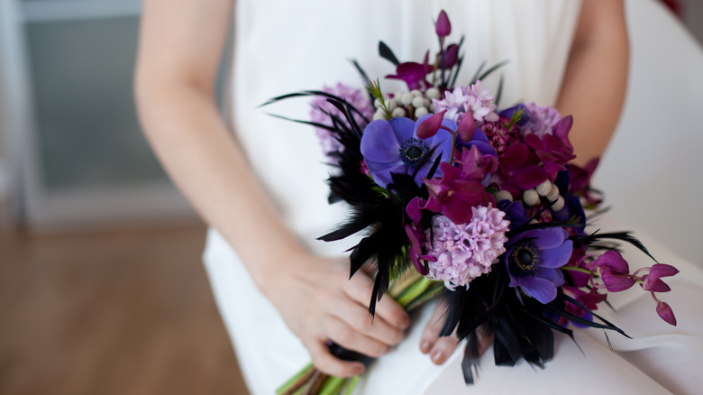 A bride is pictured holding a wedding bouquet that is a vibrant mix of bold colors in blues, purples, and pinks