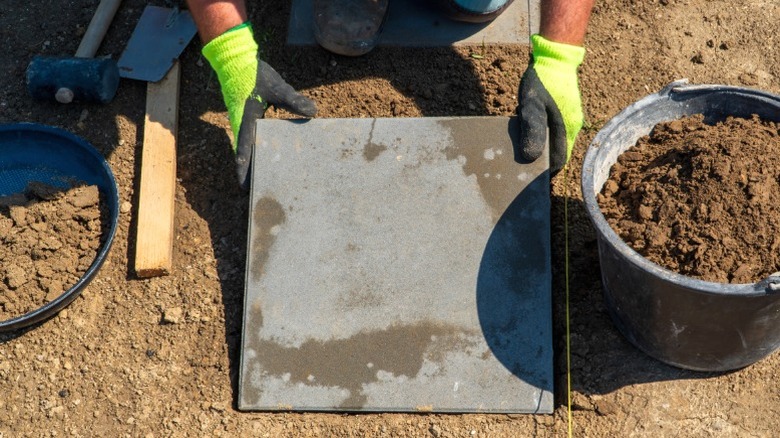 man in work gloves laying 1-foot paver pathway in prepared soil