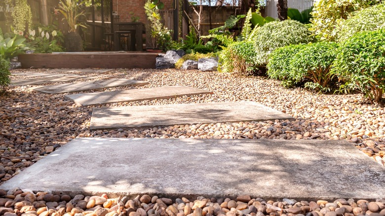 Concrete paver stepping stones surrounded by pea gravel in home garden