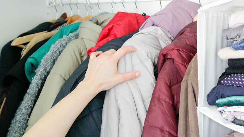 Hand reaching for winter coats in closet