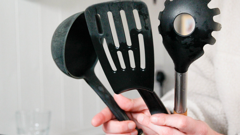 Person holding three black cooking utensils