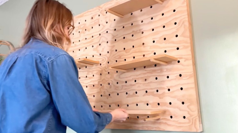 A person installing shelves on DIY giant wall-mounted pegboard