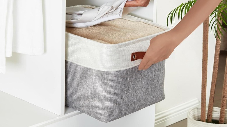 hands sliding storage bin filled with linens onto shelf