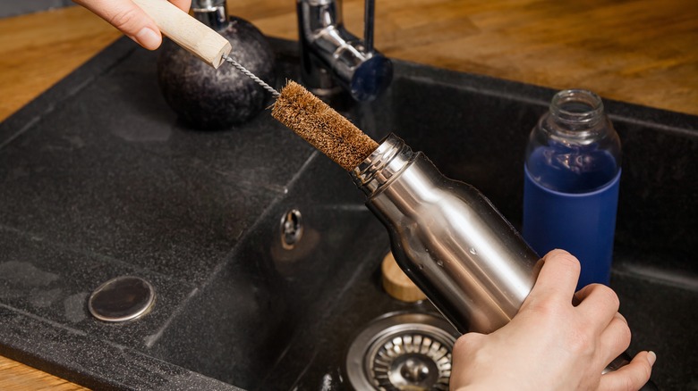 person washing reusable water bottle