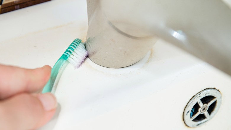 person scrubbing faucet with toothbrush