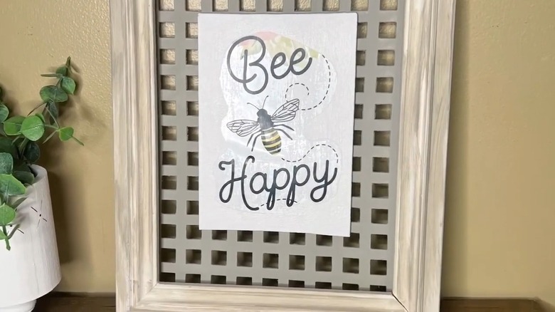 Wall art created from a frame, a painted sink mat, and an image that says "bee happy" with a bee on it.