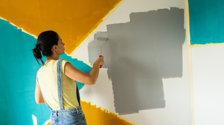 Woman painting a geometric accent wall in blue, mustard, and gray.