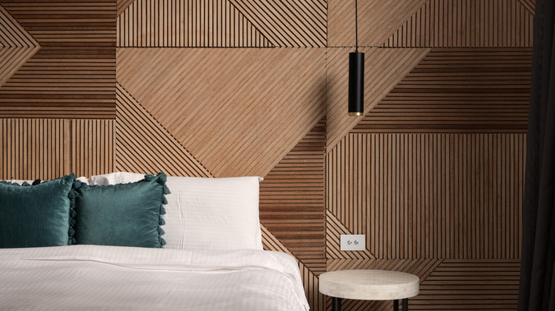 A bedroom with a white bed and geometric wood paneling as the backdrop.