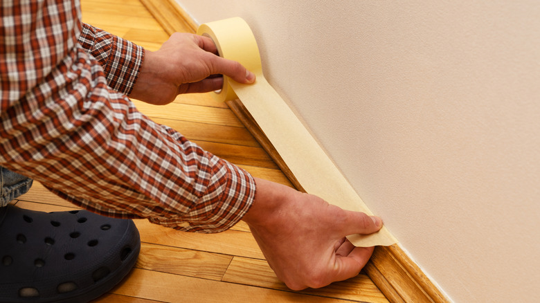  Painter glues the masking tape on wood baseboard