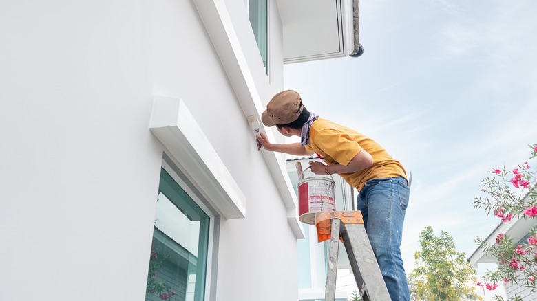 Person on a ladder painting a home exterior