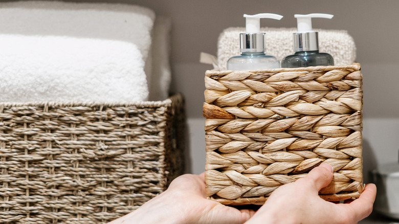 Person placing basket with towels and soap dispensers on a shelf.