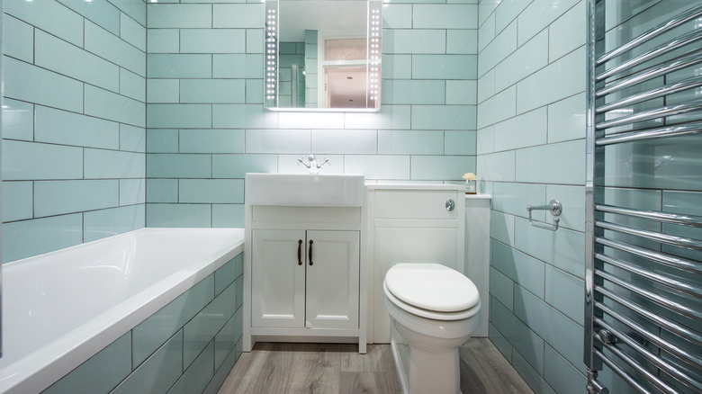 Small bathroom with a bathtub, sink, mirror, toilet, and towel drying rack.