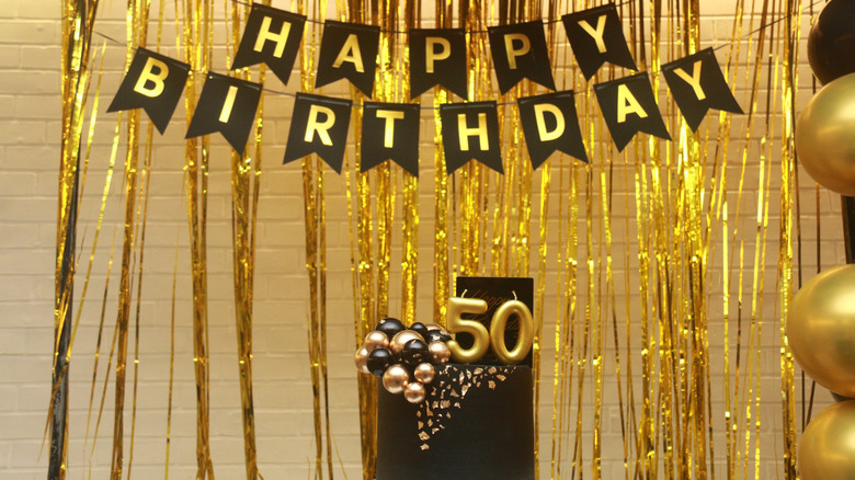 Gold foil curtains behind Happy Birthday banner and black cake