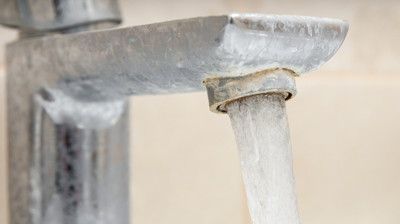 Limescale-coated sink faucet with running water