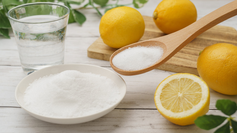 Citric acid granules being scooped from a white dish with a wooden spoon