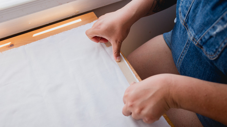 A person attaches adhesive hem tape to the cut edge of white fabric.