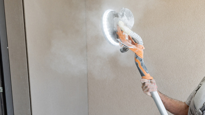 Man handling drywall sander while white dust floats everywhere