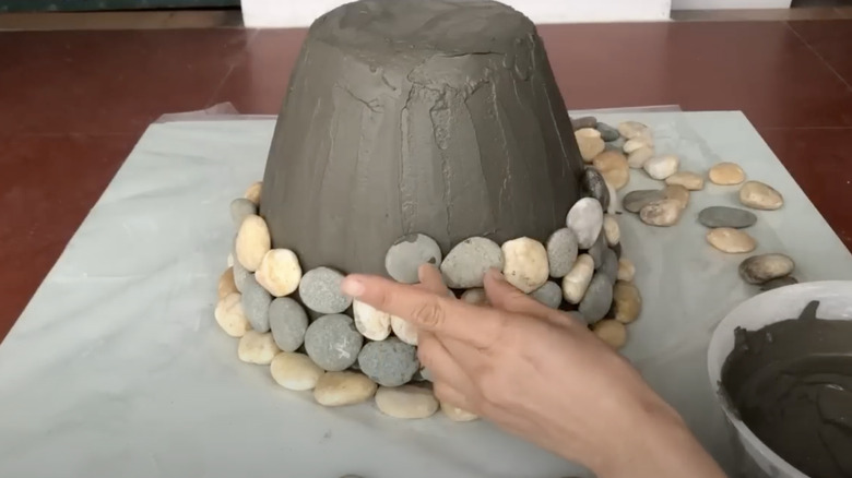 A person sticks river pebbles onto a concrete covered mold.