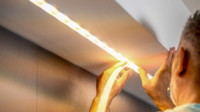 A man is adding bright white LED light strips to a ceiling bump-out.