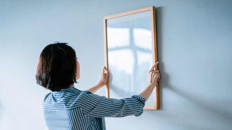 Woman hanging a framed piece of art with a glare.