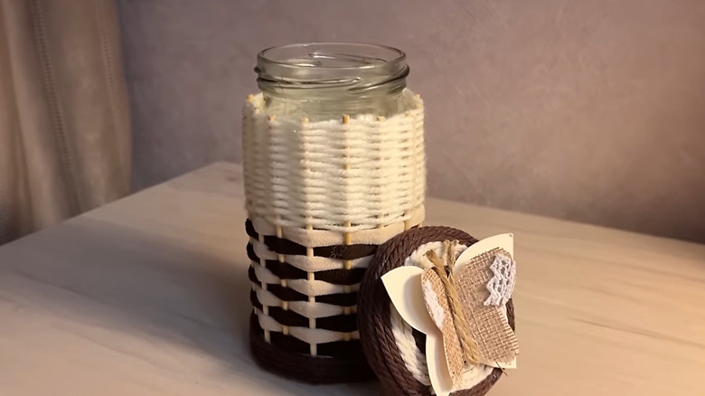 A completed woven jar with a DIY butterfly decoration on lid sits on a table