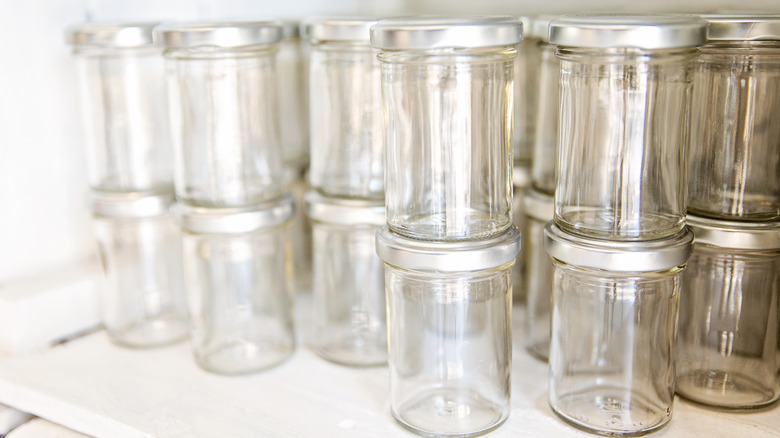 Rows of empty glass jars are stacked two tall in a cabinet