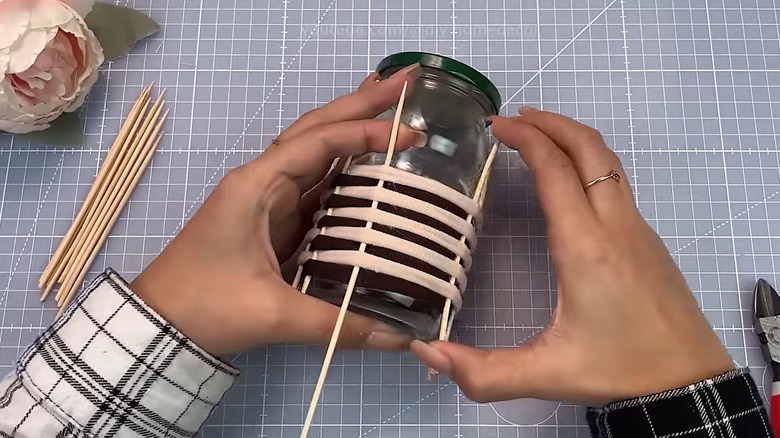 Hands holding a jar and starting the weaving process with skewers and hair ties