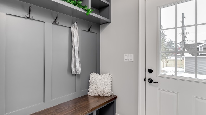 Mudroom with a butcher's block bench and coat hooks near an entryway door