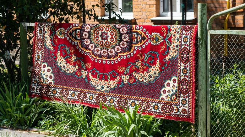 rug hanging outdoors on fence 