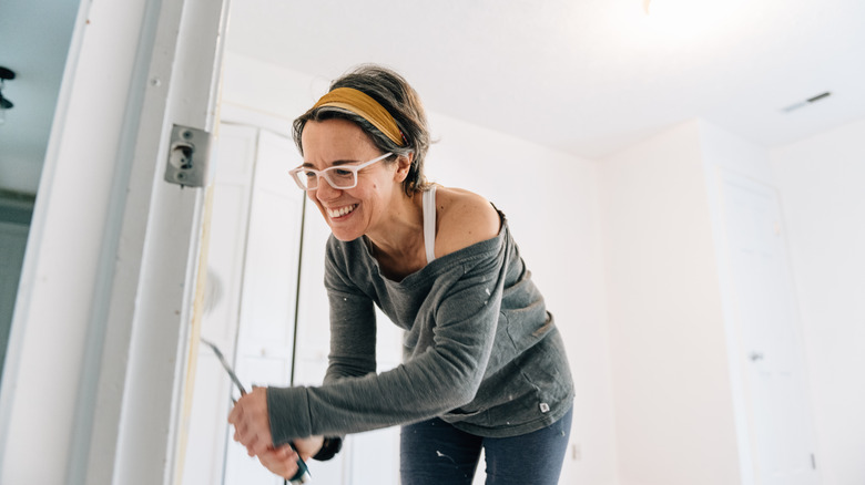 A woman smiles while painting a door trim