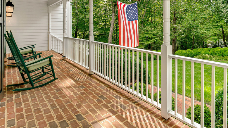 Brick front porch with green rocking chairs and American flag