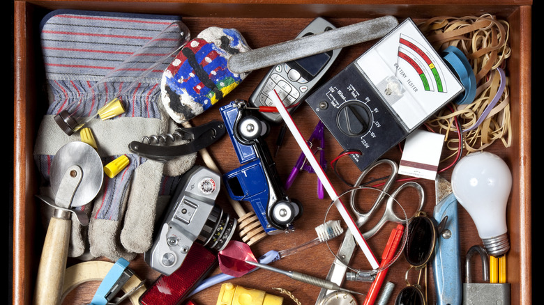 Top down view of a junk drawer with toys, straws, battery tests, and miscellaneous items