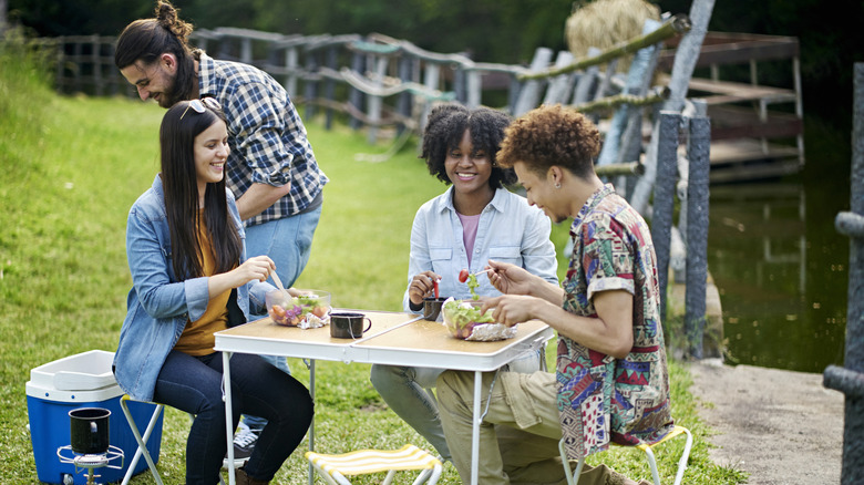 A group of young people dine on a plastic folding table outdoors