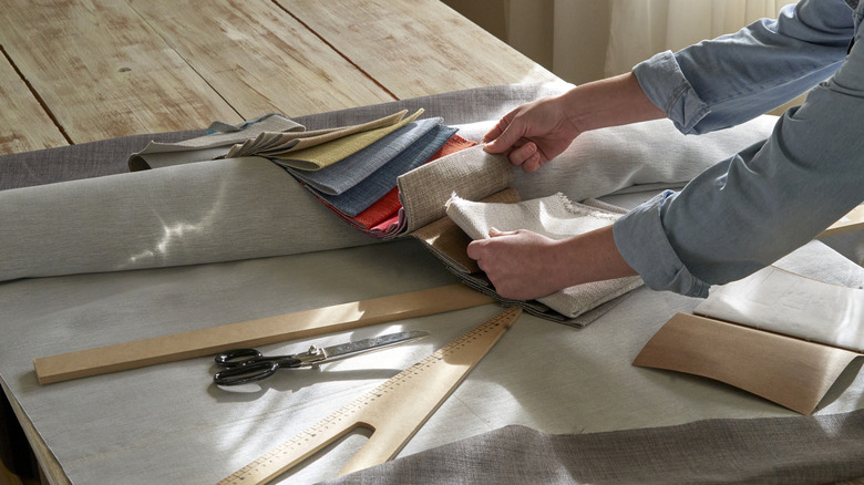 A woman selecting colored fabrics on a worktable.